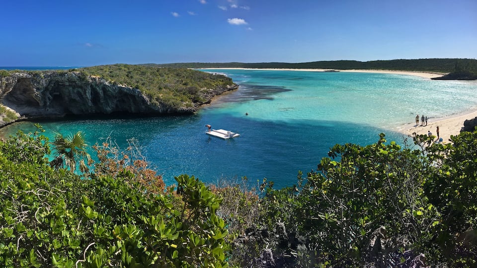 A coastal landscape with a boat on turquoise waters, a sandy beach, and lush greenery.