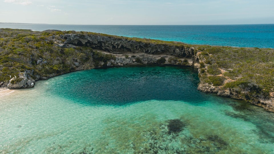 A coastal landscape with a clear turquoise sea, rocky cliffs, and sparse vegetation.
