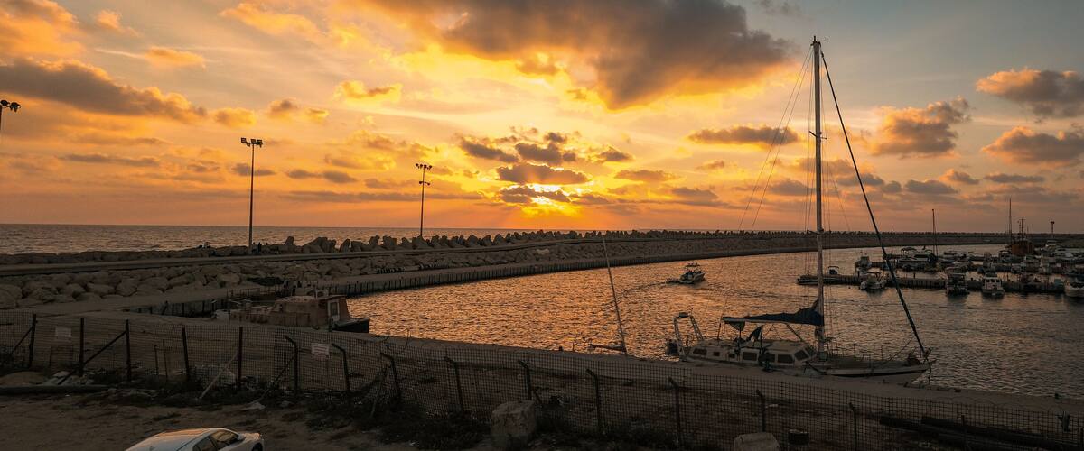 A sunset over a marina with boats and a rocky breakwater.