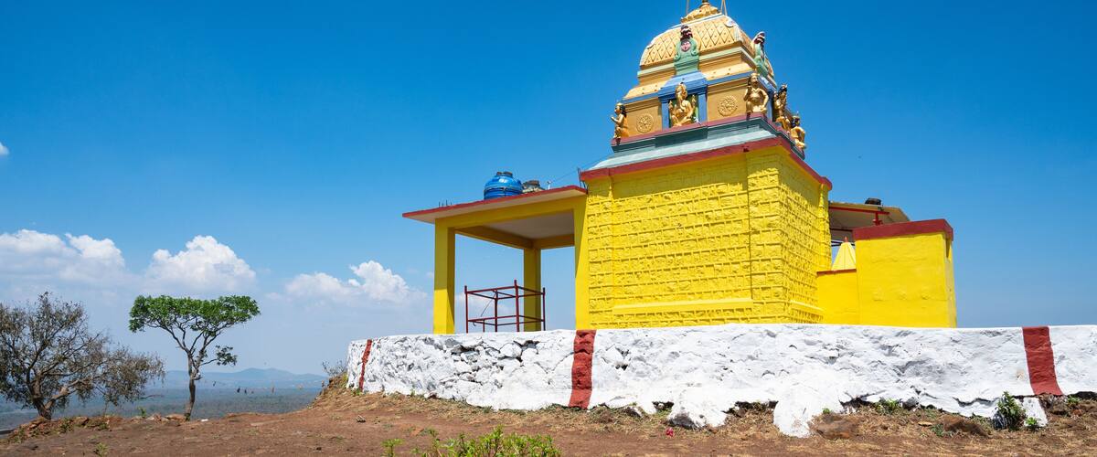 A yellow temple with a red roof and a white base, surrounded by a rocky landscape and a clear blue sky.