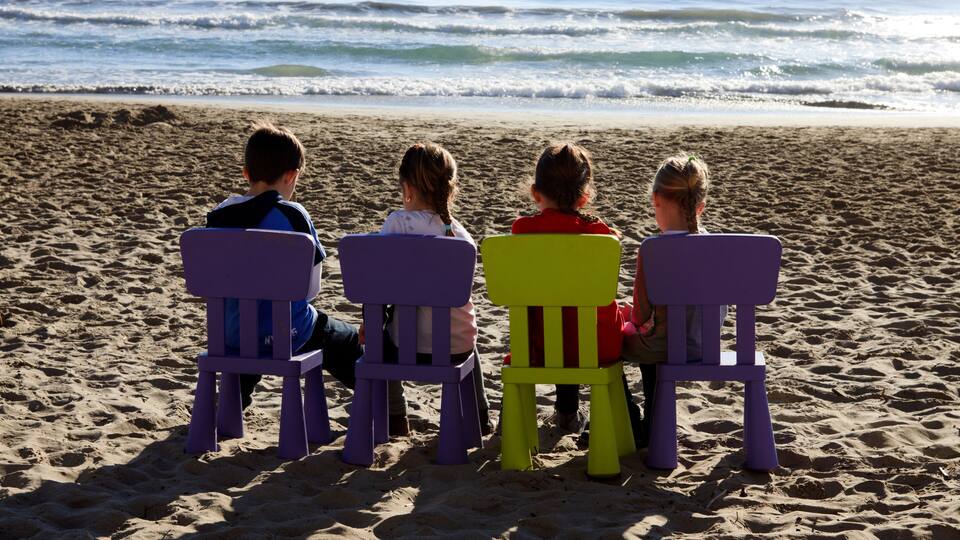 Four children sitting on beach chairs facing the ocean.