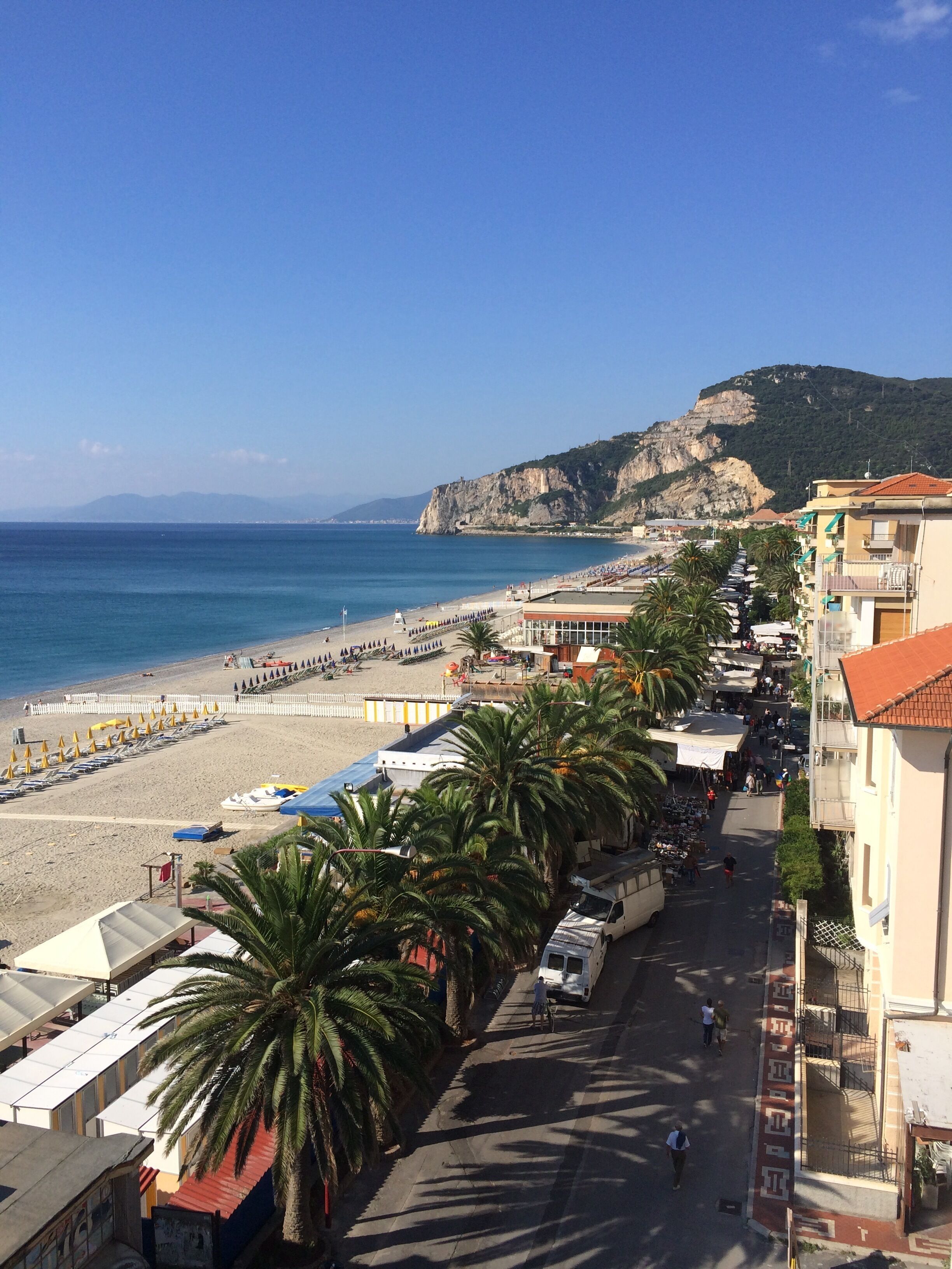 A coastal town with a beach, palm trees, and a mountain in the background.