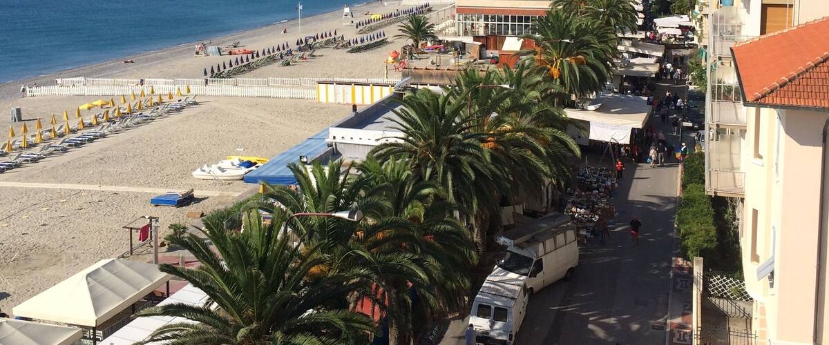 A coastal town with a beach, palm trees, and a mountain in the background.