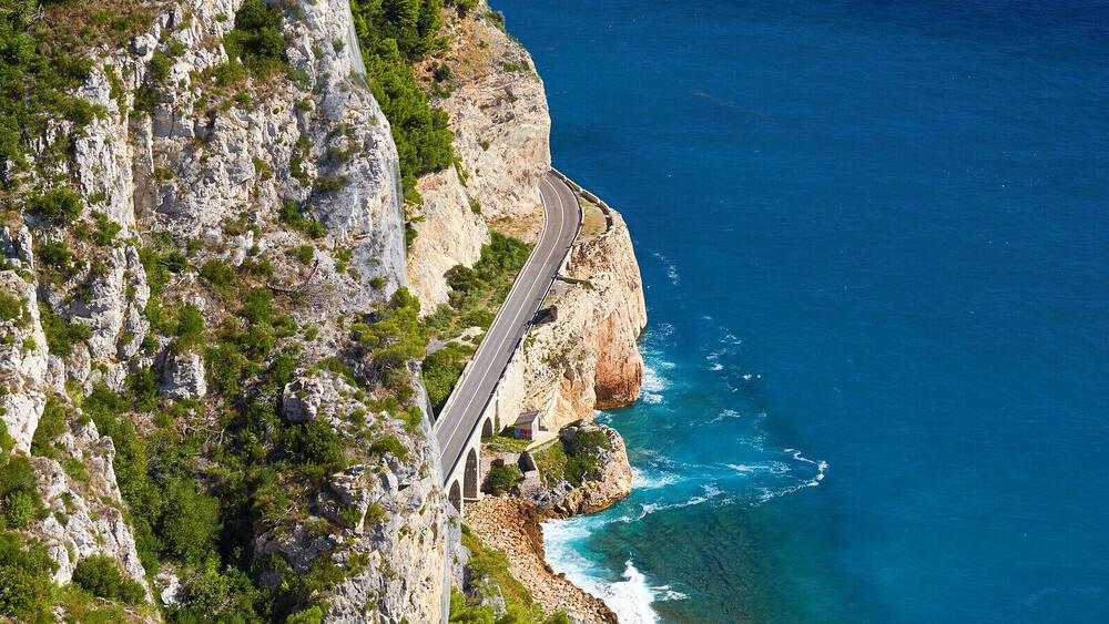 Eine Küstenstraße schlängelt sich an einer Klippe entlang, mit dem Meer im Hintergrund.