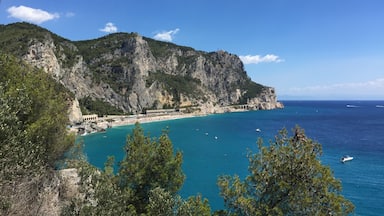 A coastal landscape with a clear blue sea, a rocky cliff, and a beach with a white building.