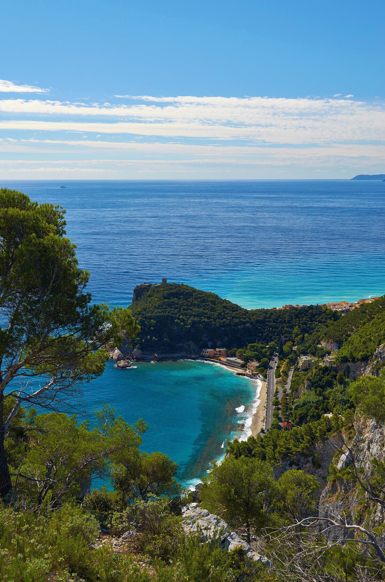 A coastal landscape with a clear blue sea, a small island with buildings, and dense green trees.
