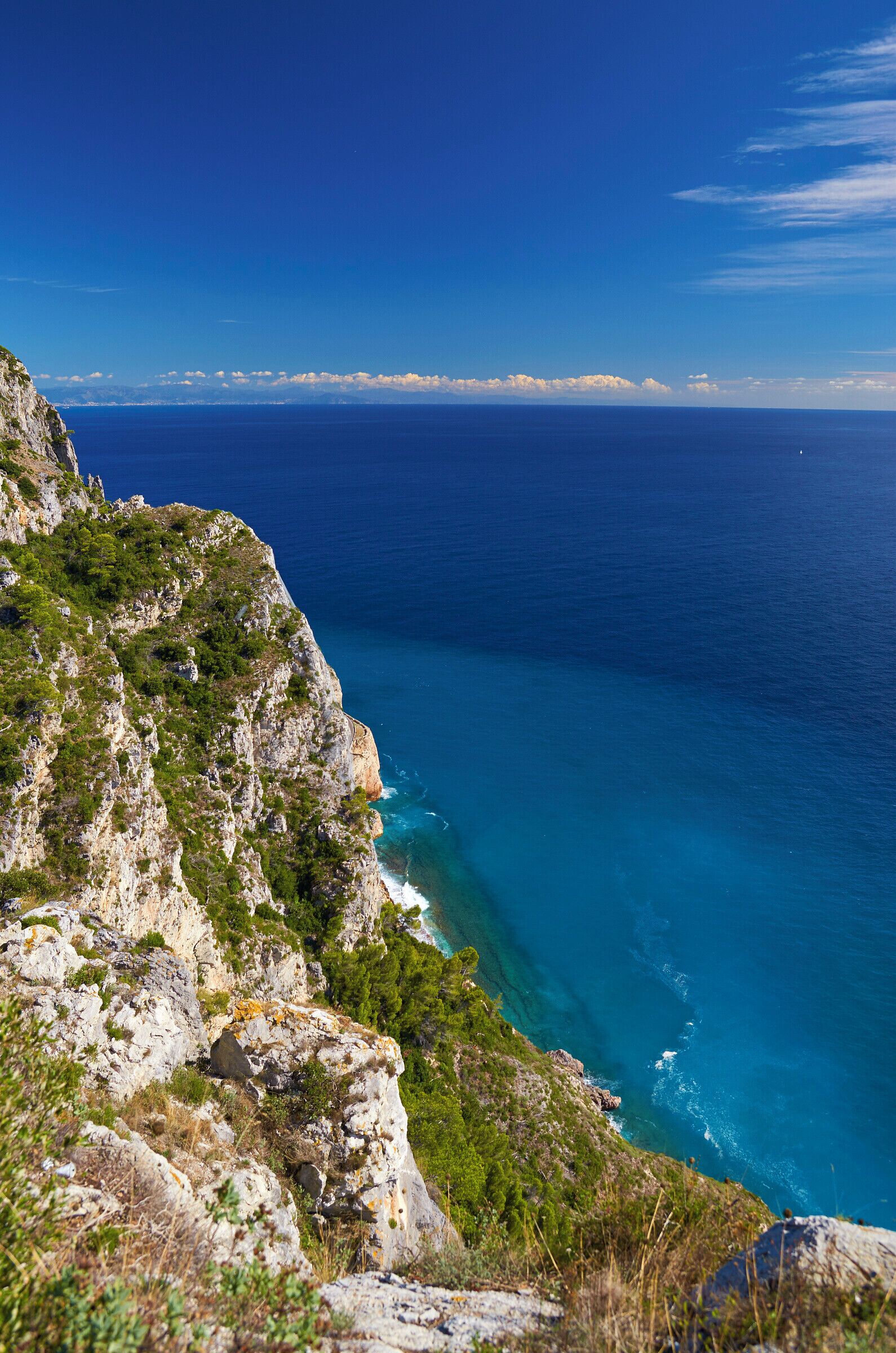 A coastal cliff with a view of the ocean and a distant shoreline.