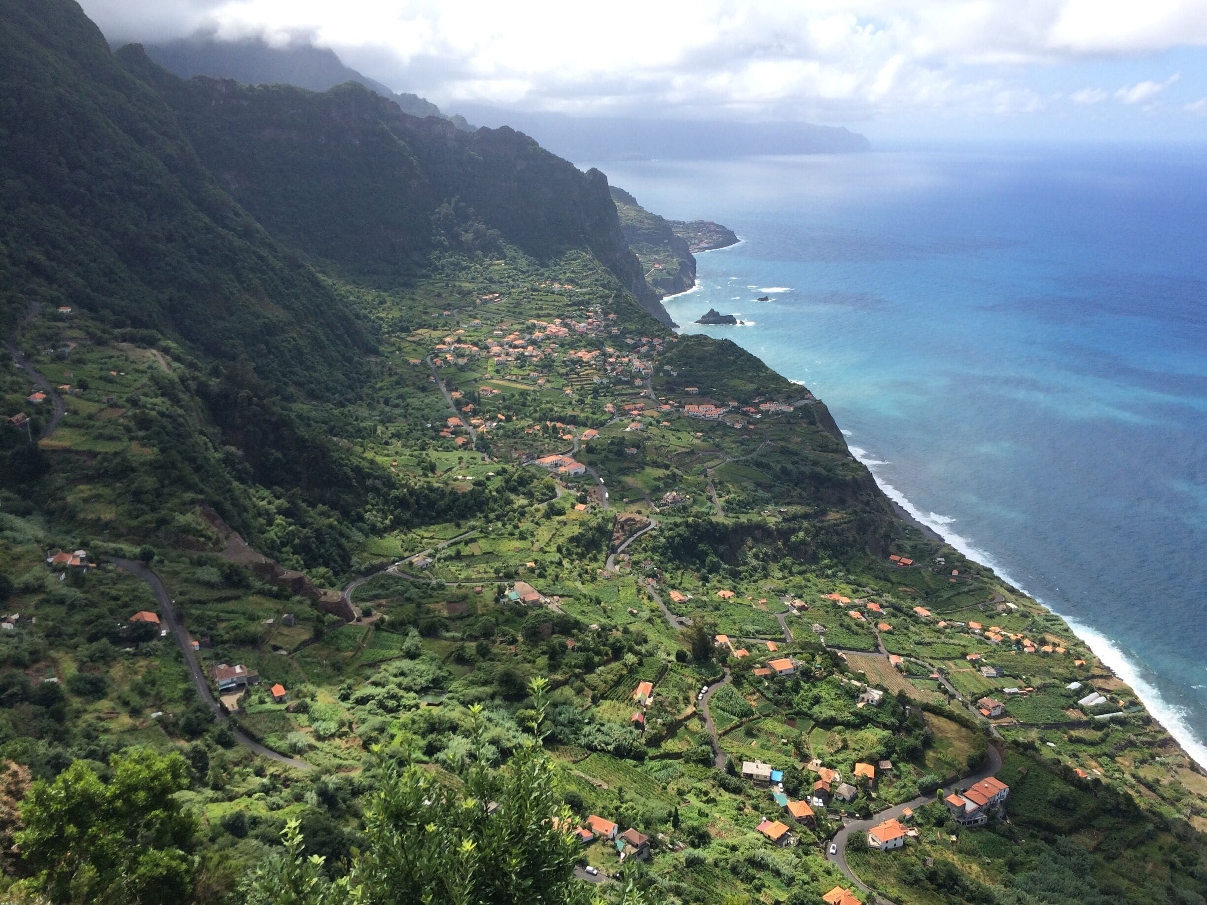 A coastal village nestled in lush green hills with a view of the ocean.
