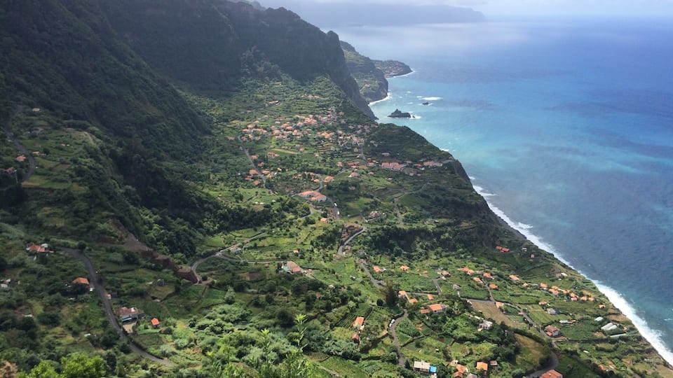 A coastal village nestled in lush green hills with a view of the ocean.