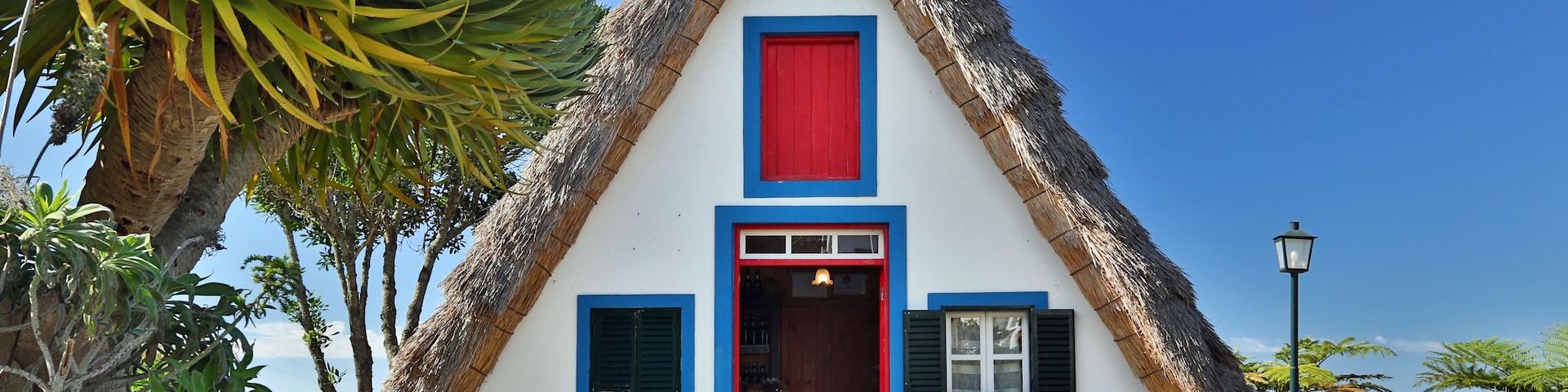 A traditional thatched-roof house with a red door, blue shutters, and a white facade.