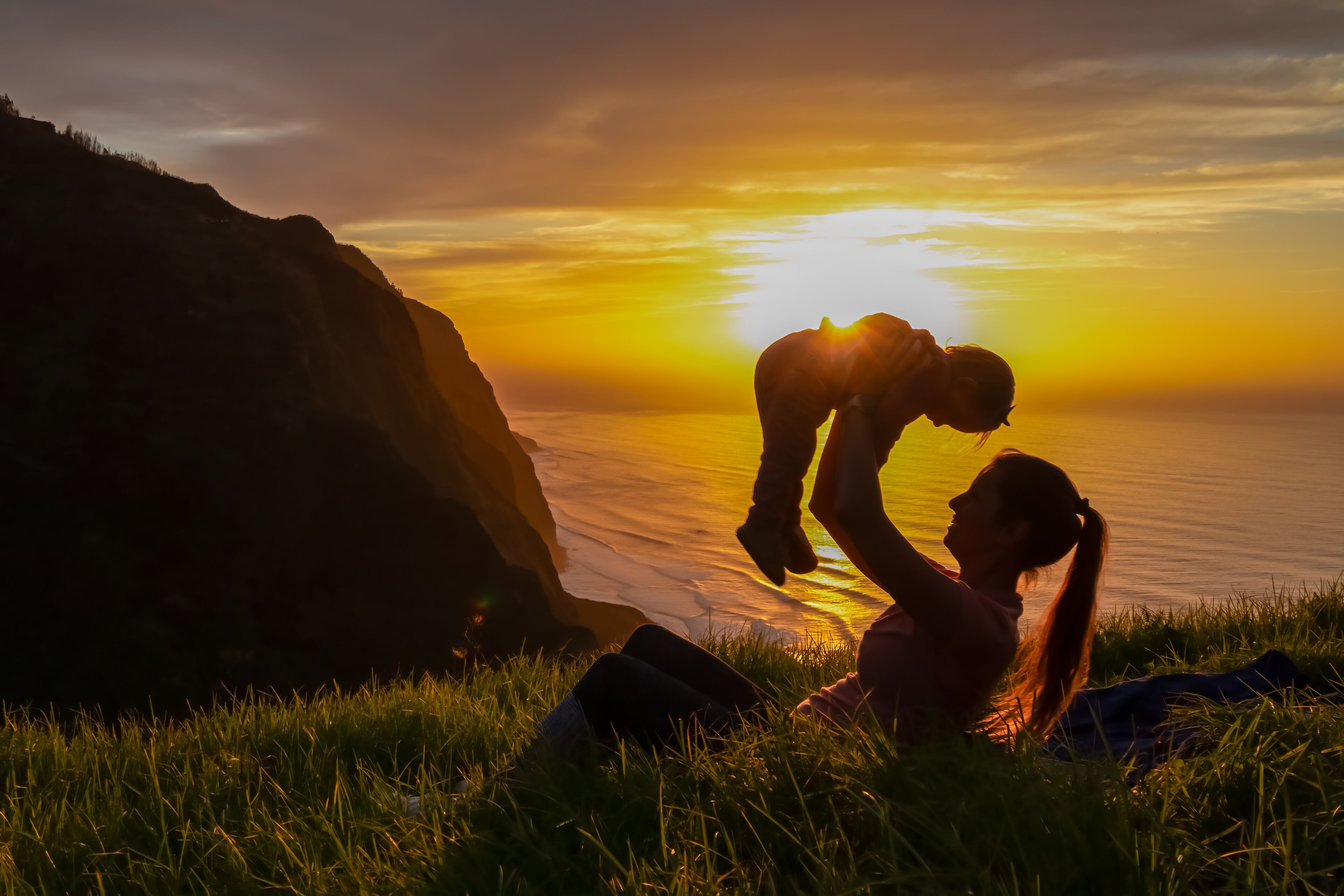 Um pôr do sol sobre uma paisagem costeira com uma pessoa sentada na grama.