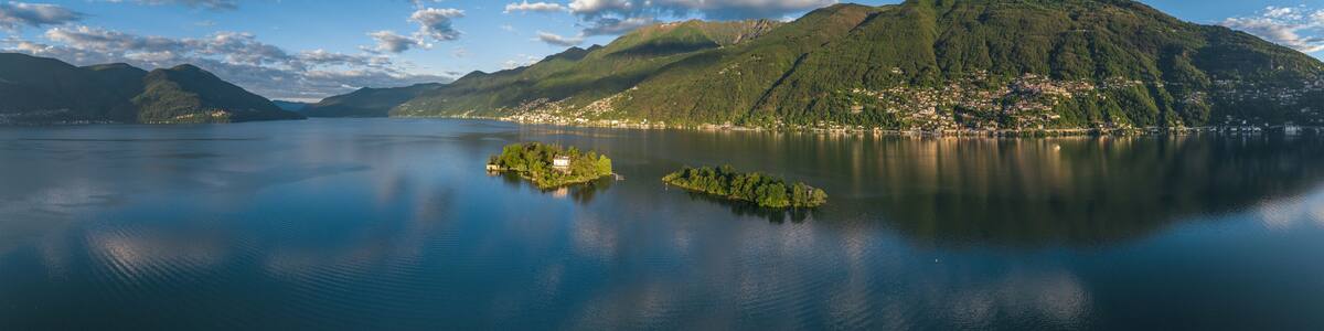 A calm lake with a small island, mountains in the background, and a clear sky.
