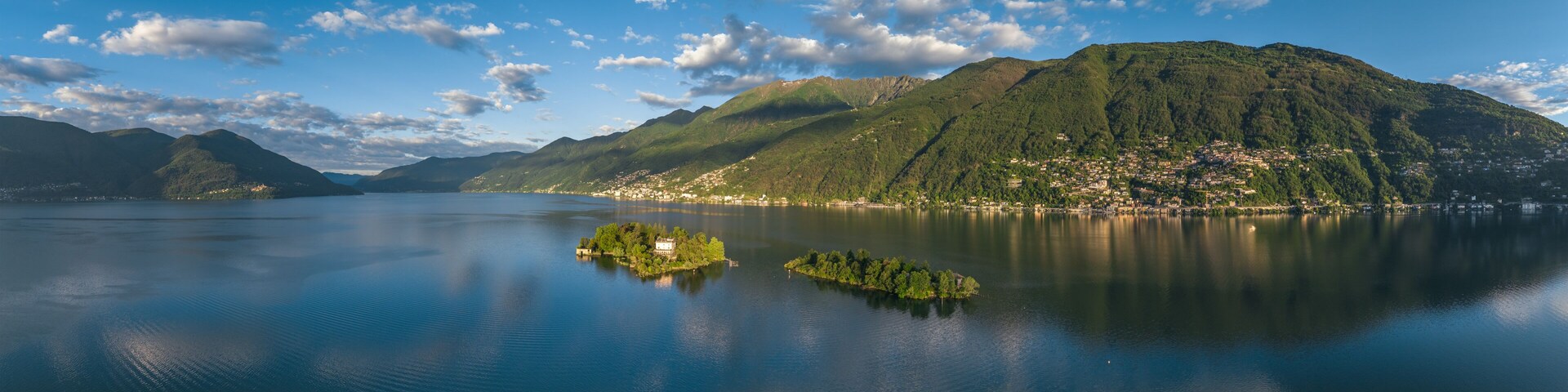 Un lago sereno con una pequeña isla, montañas al fondo y un cielo despejado.