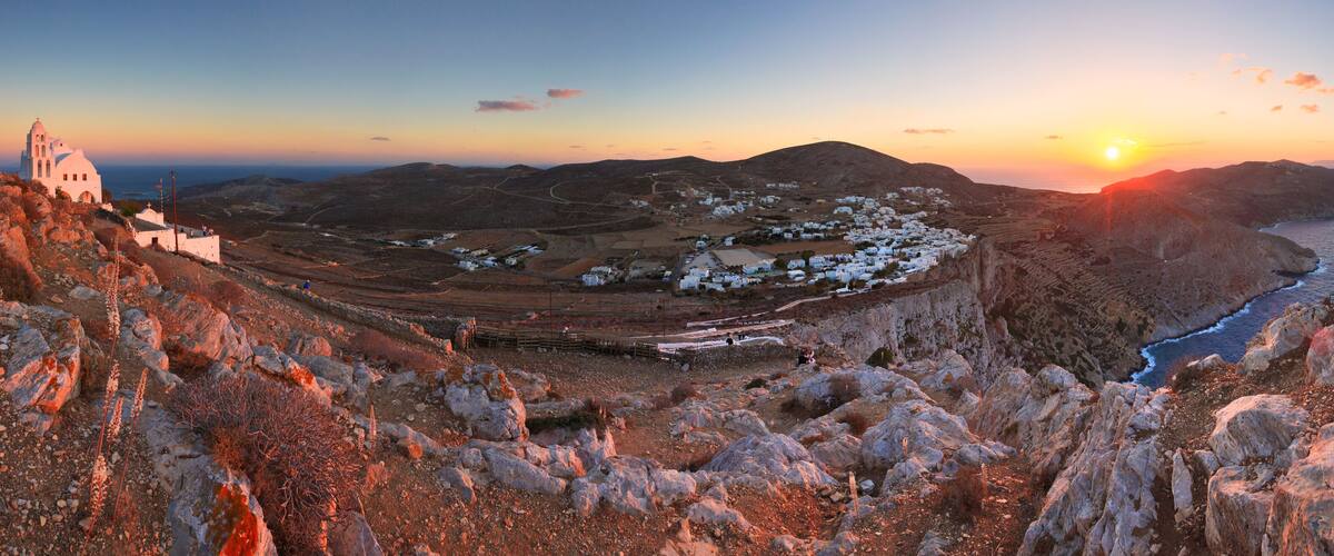 A coastal village with white buildings, a church, and a rocky landscape during sunset.