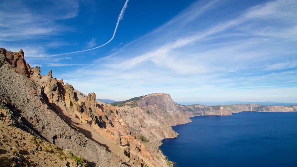 A rugged coastline with a clear blue sky and a visible contrail.