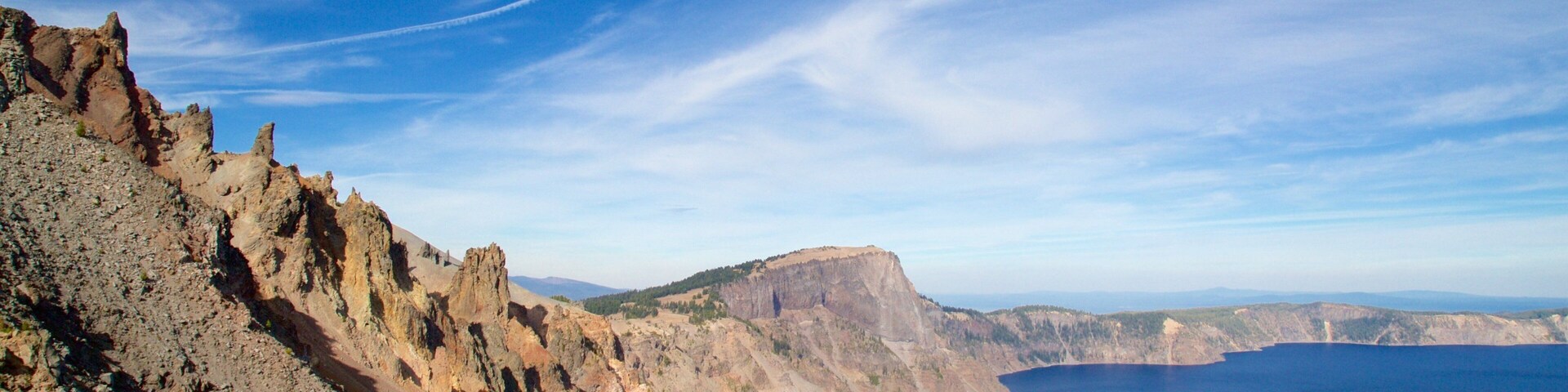 A rugged coastline with a clear blue sky and a visible contrail.