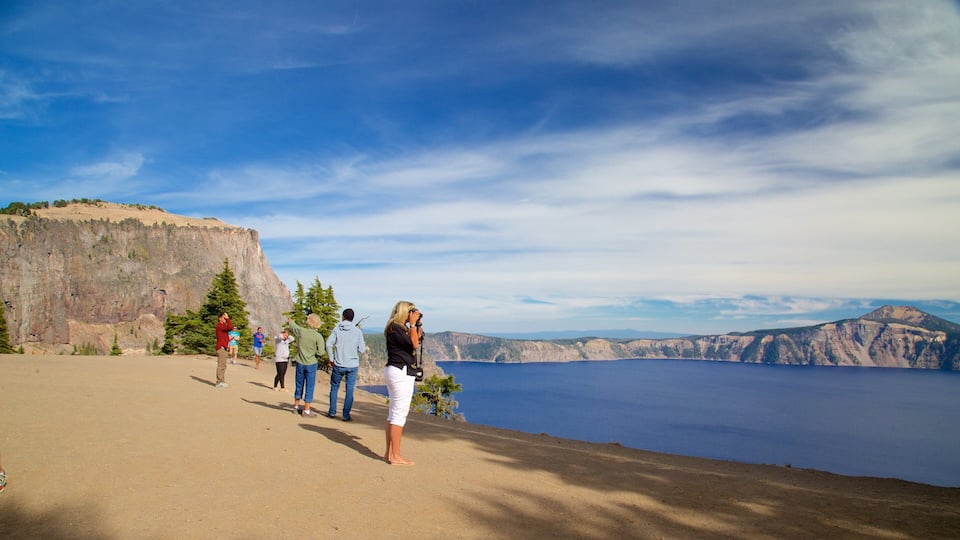 A group of people on a dirt path overlooking a large body of water and a cliff.