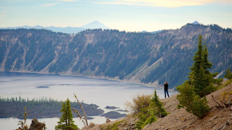 A person standing on a rocky outcrop overlooking a lake with mountains in the background.