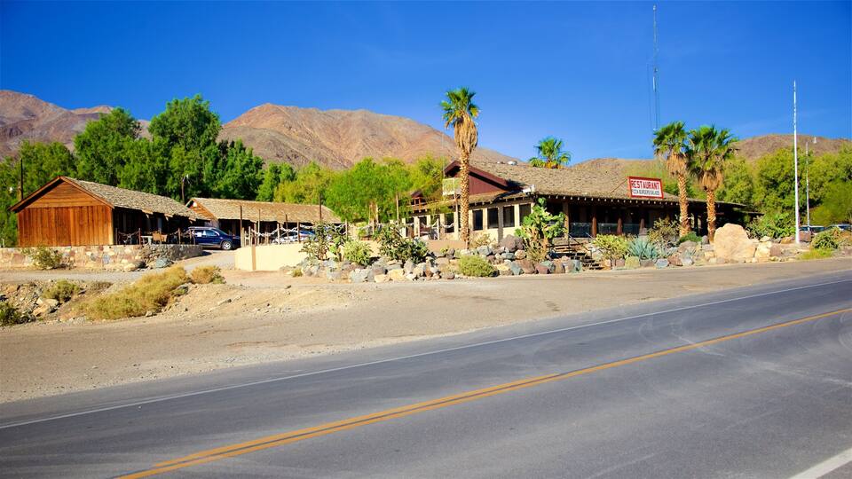 A desert landscape with a road, a wooden building, a restaurant, and mountains in the background.