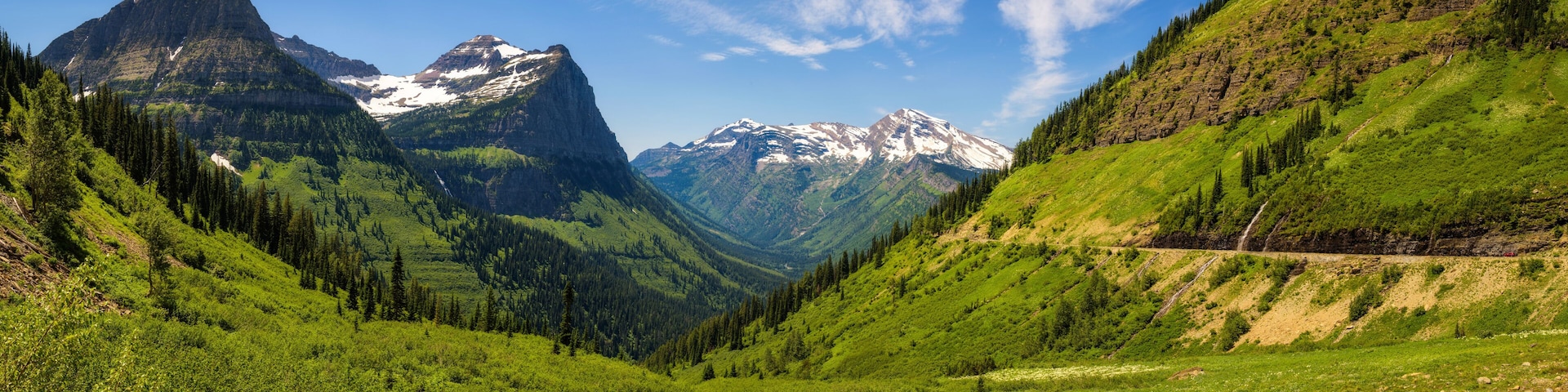 Un paisaje montañoso con un valle, bosques densos y cumbres nevadas.