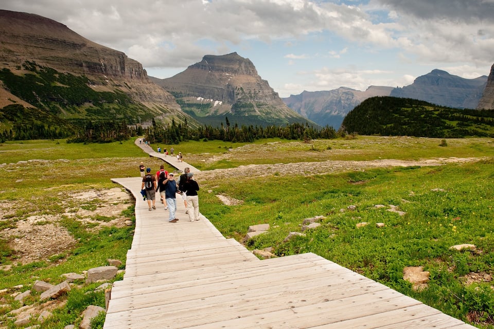 A wooden boardwalk in a mountainous area with hikers.