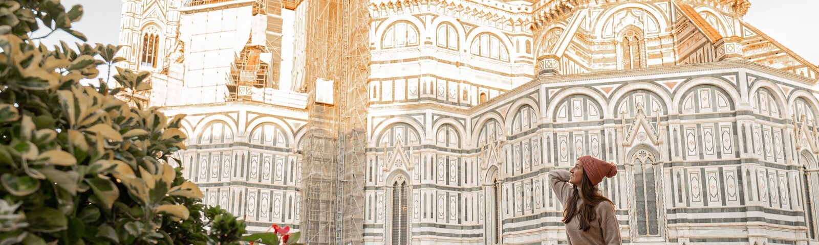 Una catedral histórica con arquitectura elaborada, una persona cargando a otra, y plantas en macetas al frente.