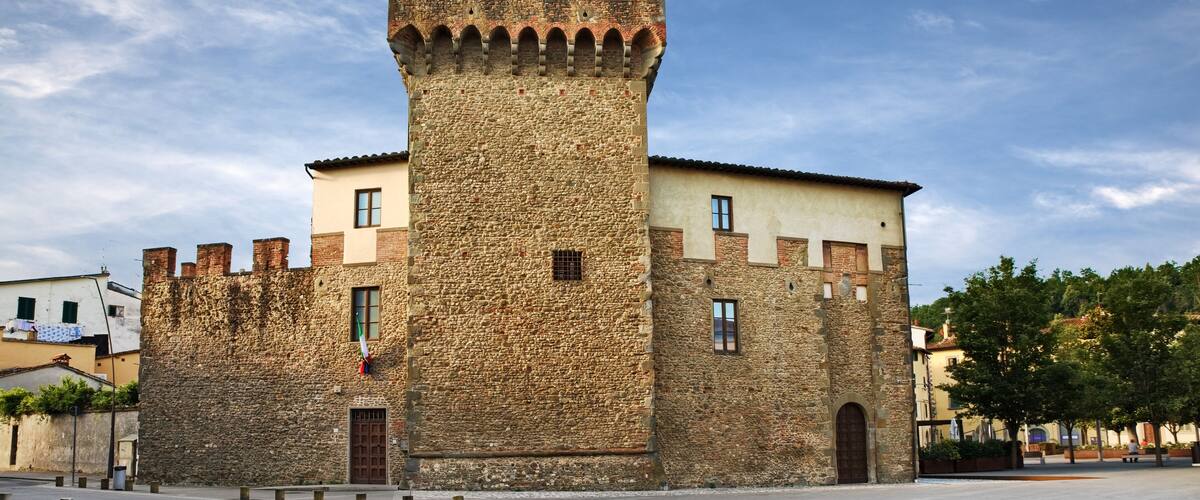 A historic stone tower with a crenellated top, adjacent to a building with a tiled roof.