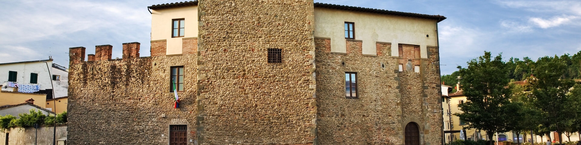 A historic stone tower with a crenellated top, adjacent to a building with a tiled roof.
