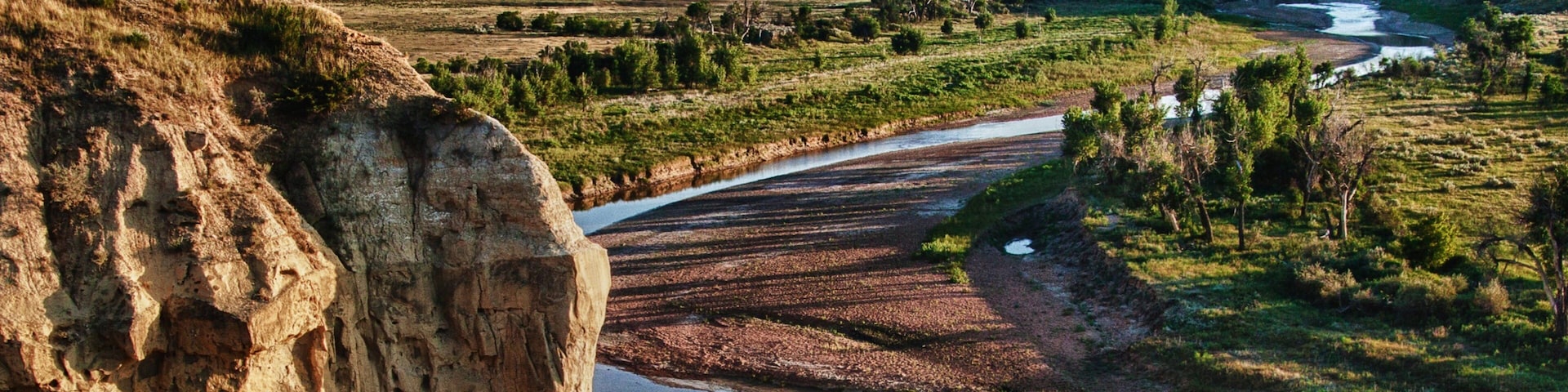 Um rio serpenteando por um vale com penhascos rochosos e vegetação rala.