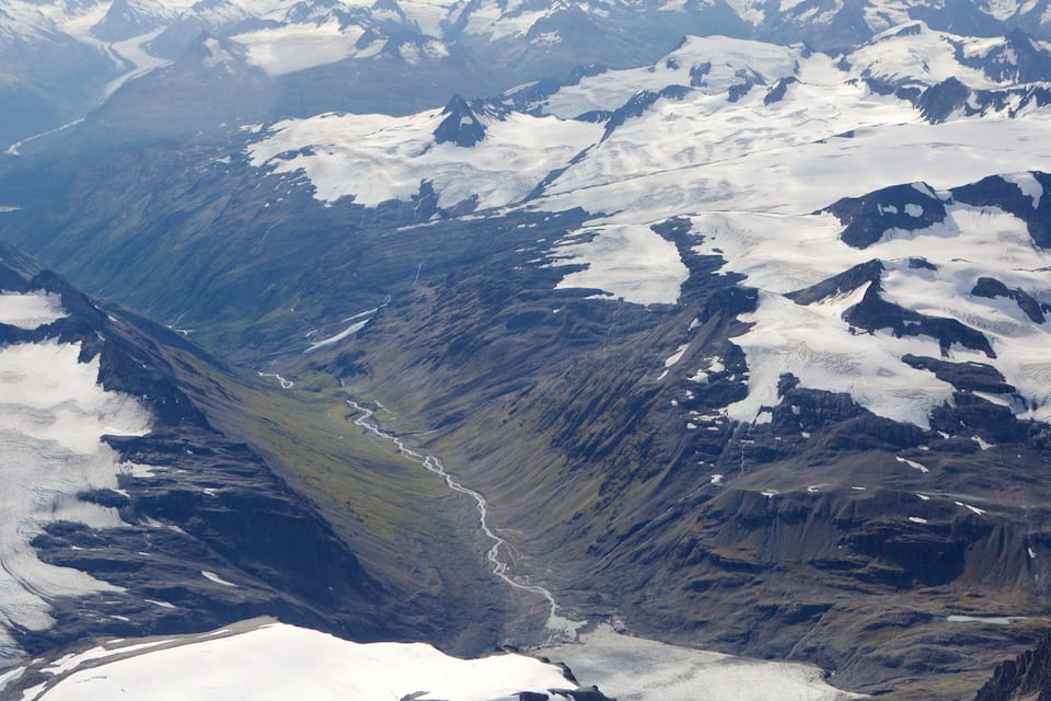 A mountainous landscape with snow-covered peaks and a river winding through a valley.
