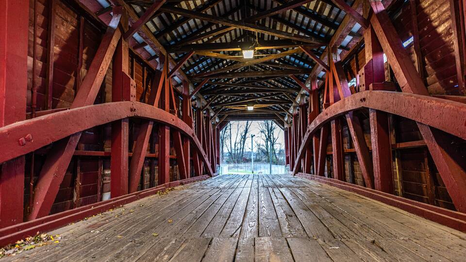 A covered wooden bridge with red metal beams and a wooden floor.