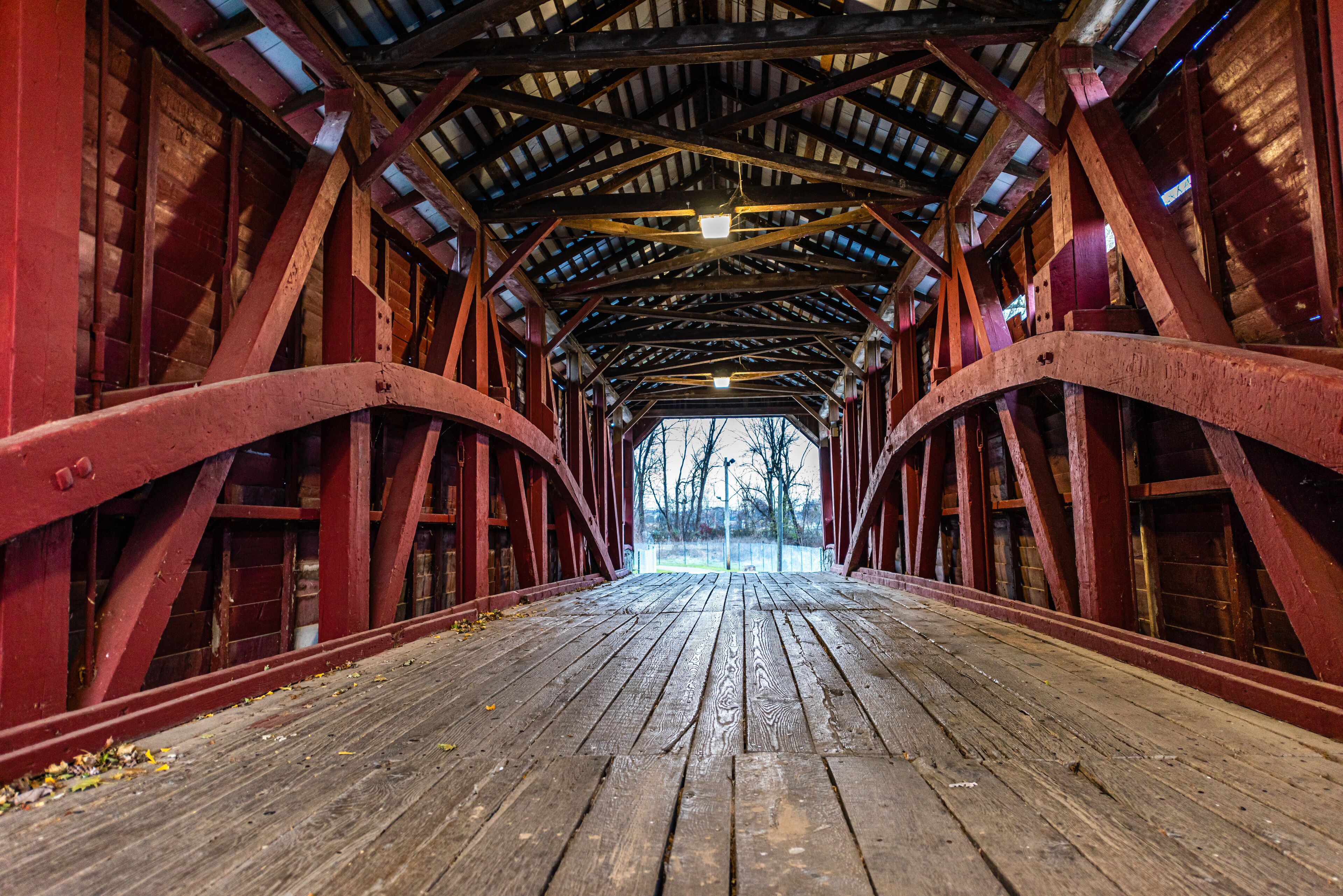 A covered wooden bridge with red metal beams and a wooden floor.