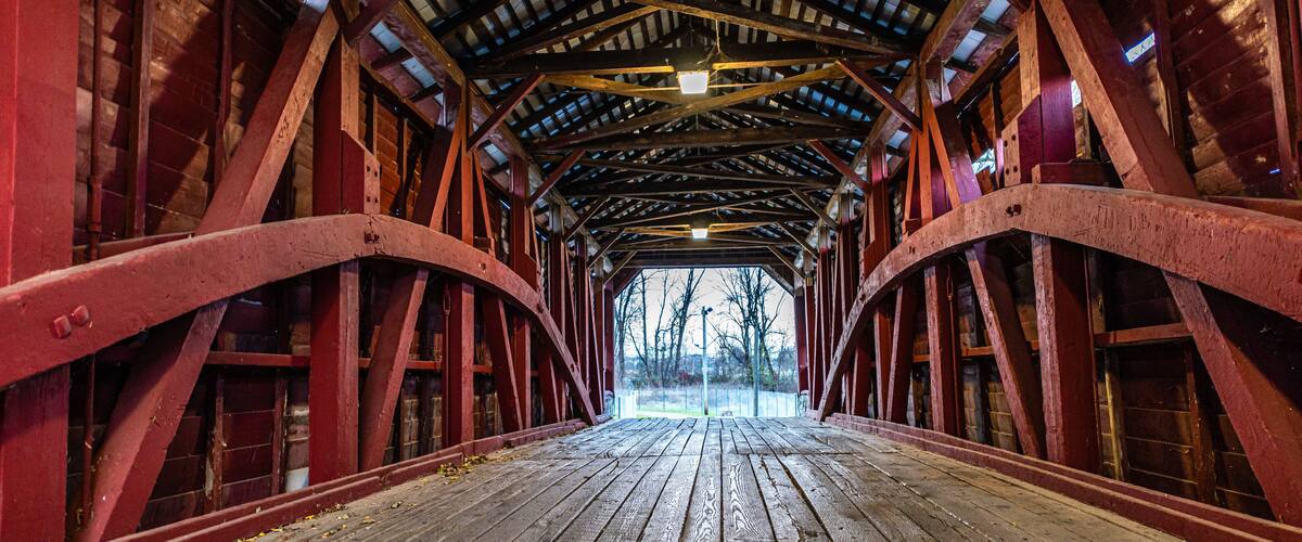 A covered wooden bridge with red metal beams and a wooden floor.