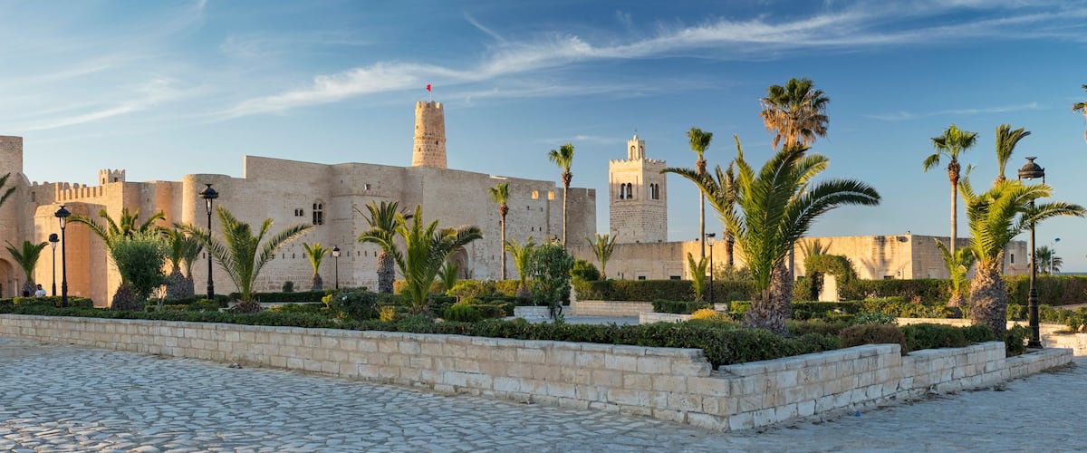 A historic stone fortress with palm trees and cobblestone pathways.