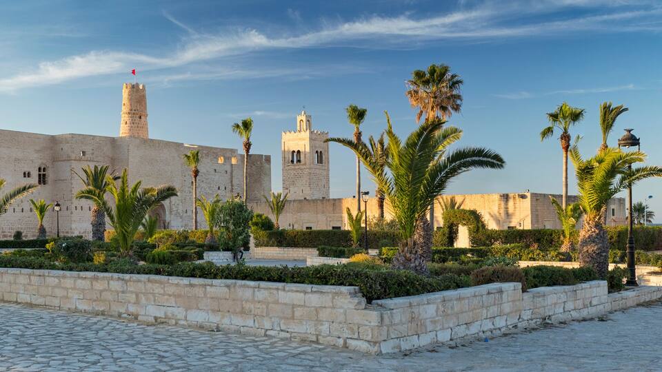 A historic stone fortress with palm trees and cobblestone pathways.