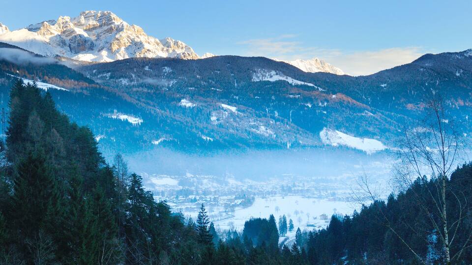 A mountainous landscape with snow-covered peaks and a valley with dense forests.