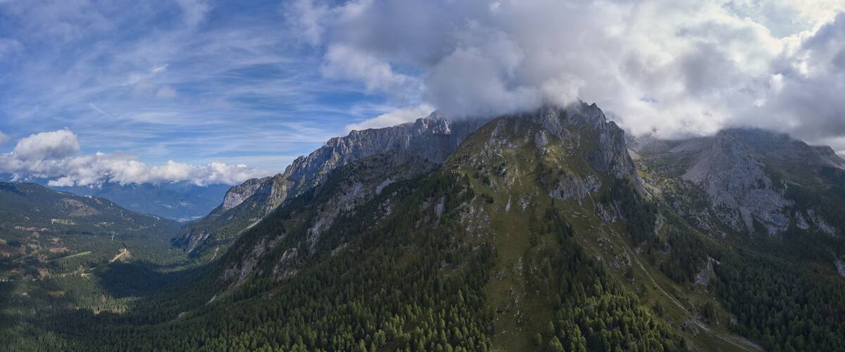 A mountain peak with a forested valley and a cloudy sky.