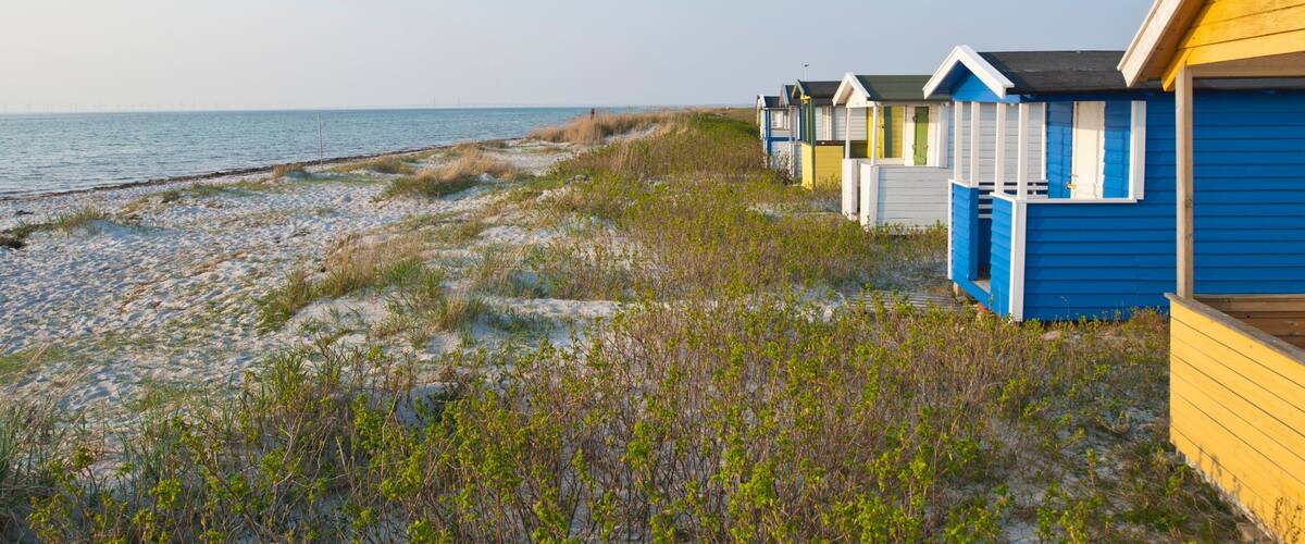 A beach with sand dunes and a row of colorful beach huts.