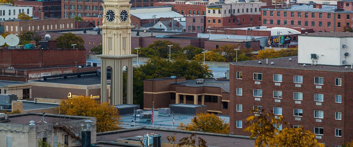 A cityscape with a prominent clock tower, a mix of red and white buildings, and a highway in the background.