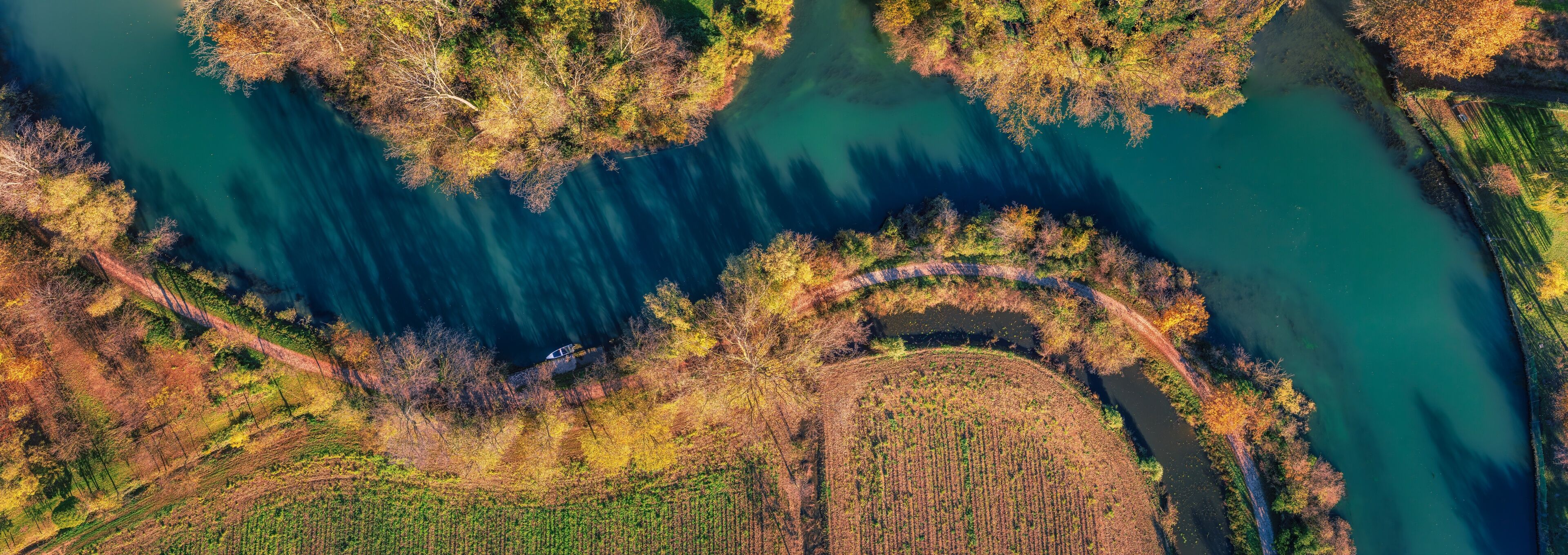 An aerial view of a river winding through a forested area with clearings and agricultural fields.