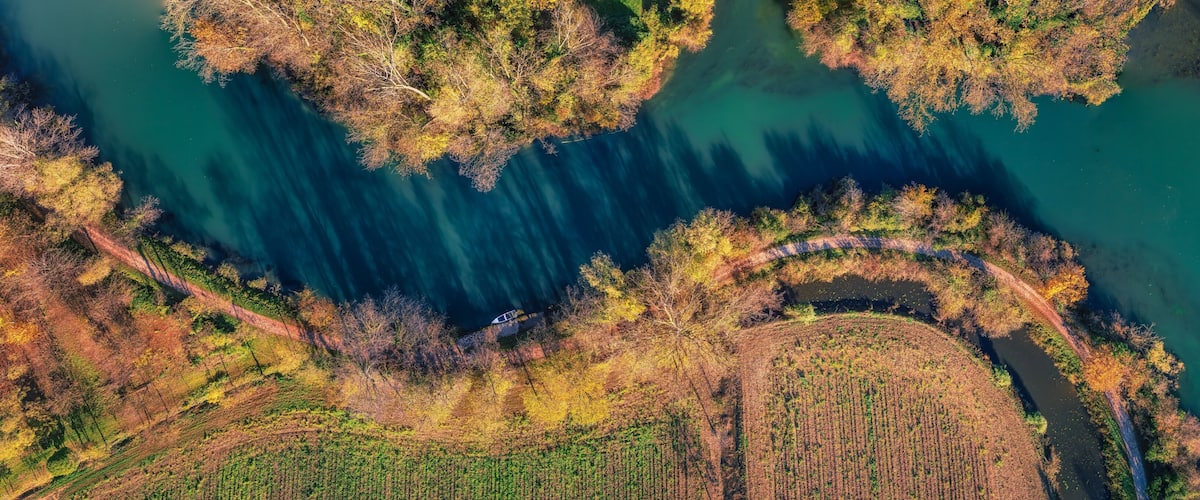 An aerial view of a river winding through a forested area with clearings and agricultural fields.