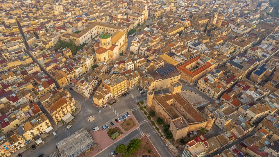 An aerial view of a densely packed urban area with historic architecture, including a prominent church with a green dome and a large tower.