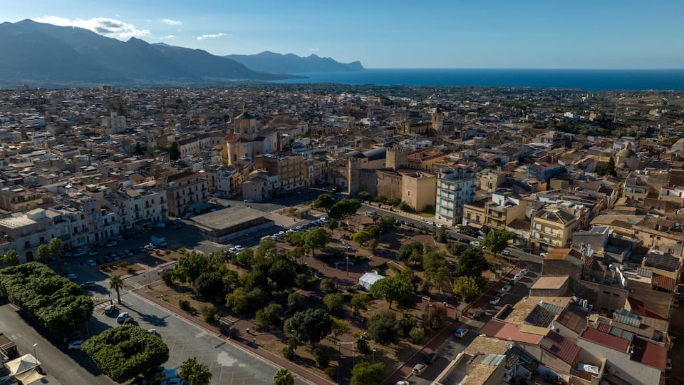 A coastal cityscape with dense urban architecture, a prominent church, and mountains in the background.