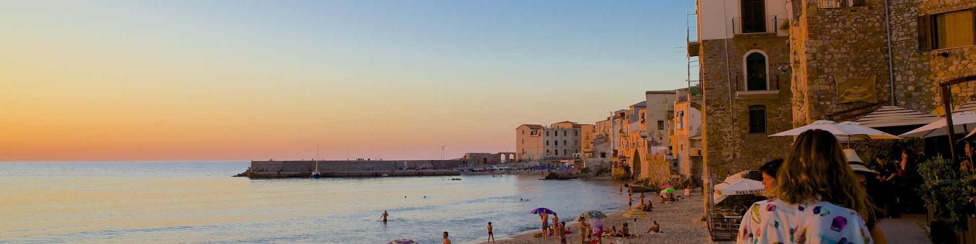 Una playa al atardecer con gente, sombrillas y edificios a lo largo de la costa.