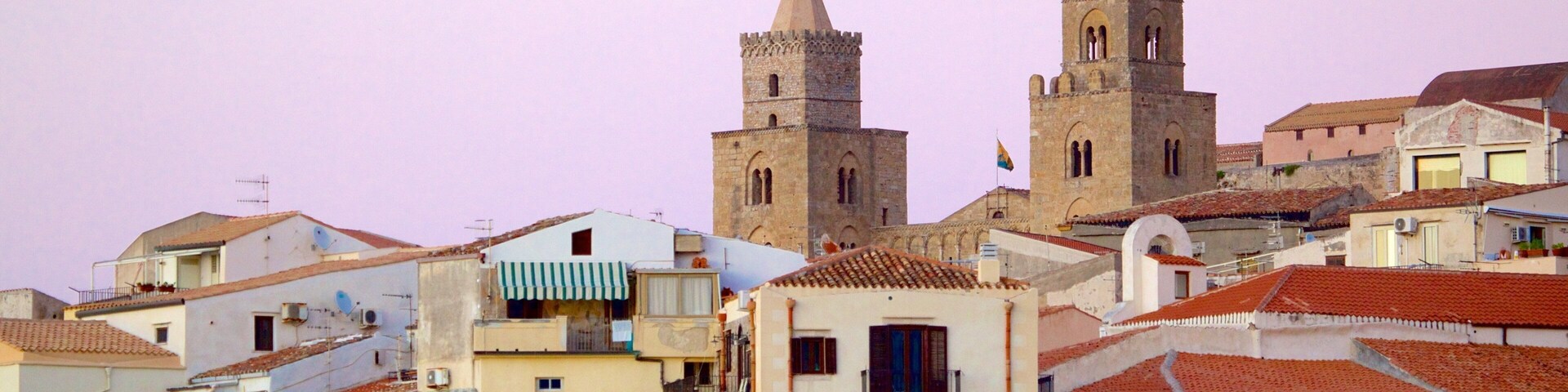 Un pueblo histórico con edificios de piedra, tejados de tejas rojas y dos torres destacadas.