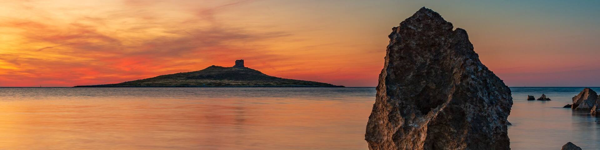 A rock formation in the foreground with a sunset in the background.