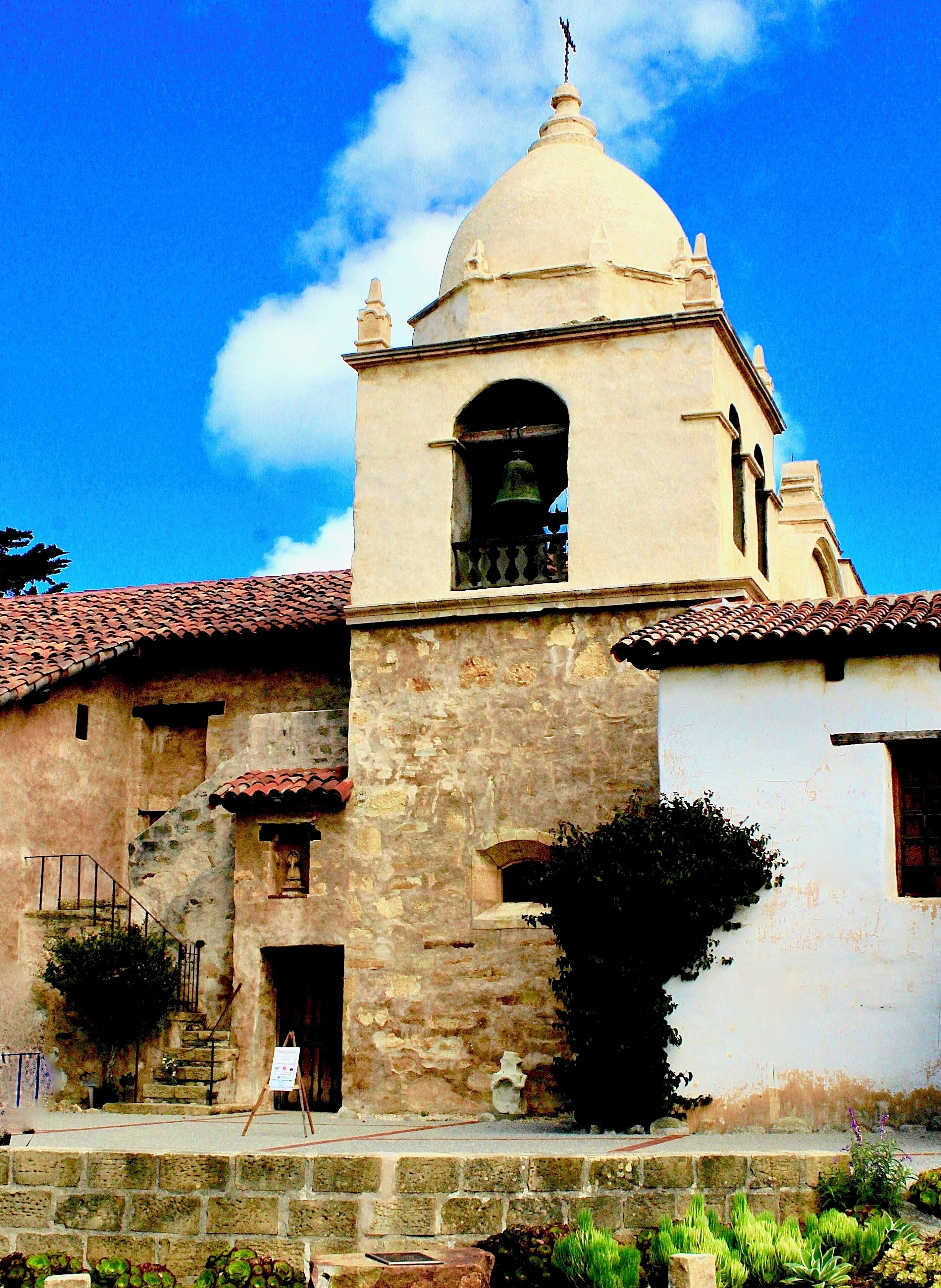 A historic building with a bell tower and a dome, surrounded by stone walls and a tiled roof.