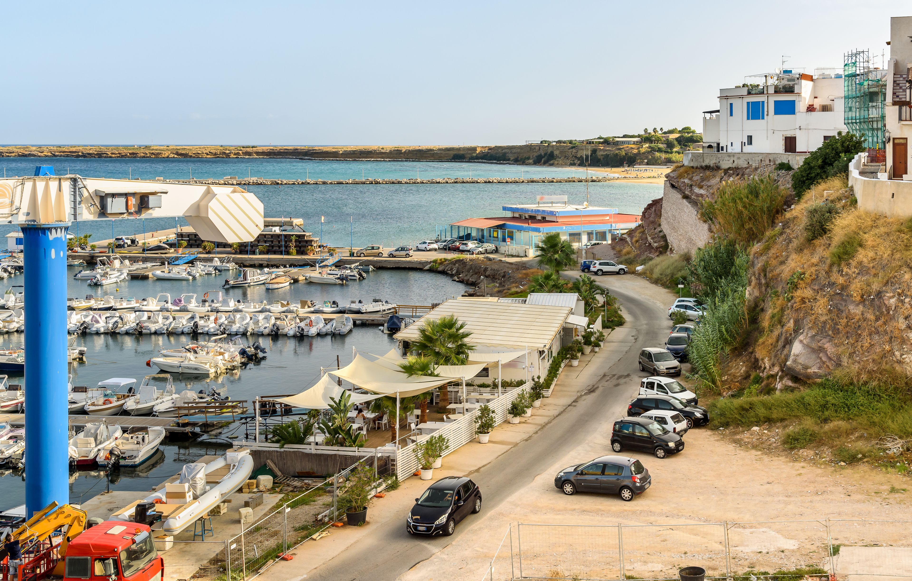 A coastal marina with boats, a road, and buildings.