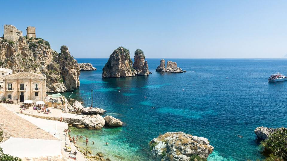 Une ville côtière dotée de bâtiments historiques, de falaises rocheuses, d’une mer d’un bleu limpide et de bateaux.
