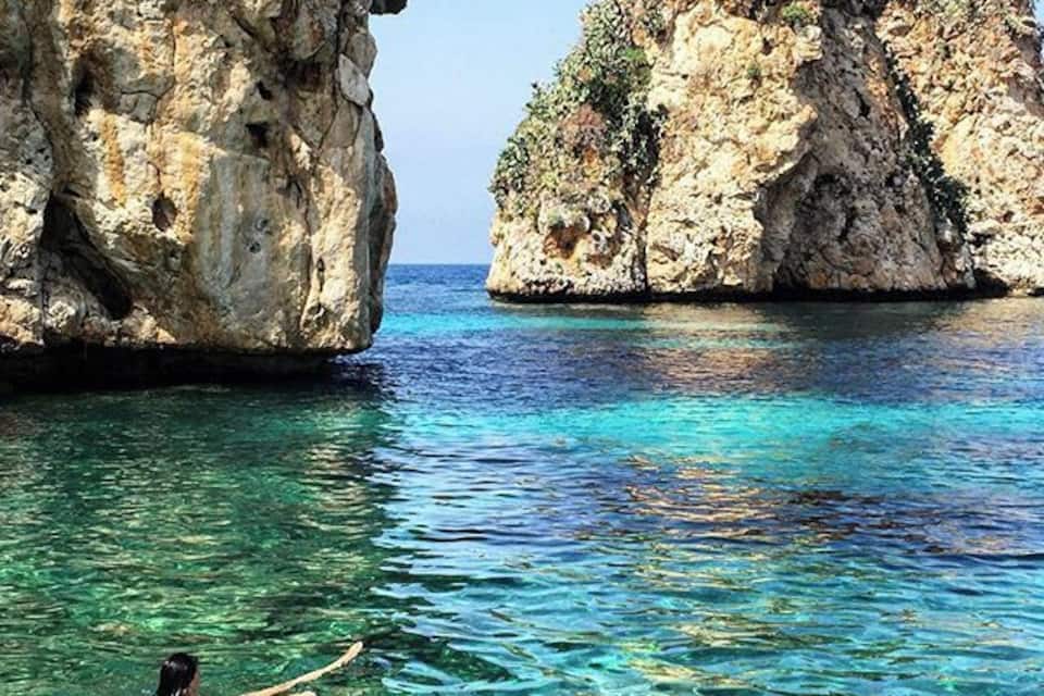 Un banyador a l'aigua turquesa cristal·lina amb penya-segats rocosos al fons.
